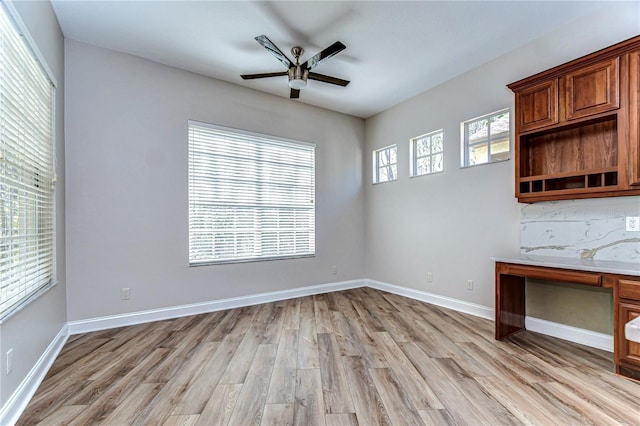 interior space featuring light wood-type flooring, baseboards, a ceiling fan, and built in study area