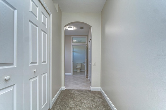 hallway with arched walkways, carpet flooring, visible vents, and baseboards