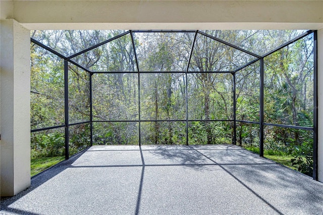 view of patio / terrace featuring glass enclosure and a wooded view