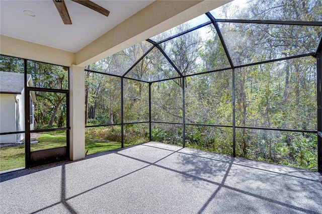 unfurnished sunroom with ceiling fan and a wooded view