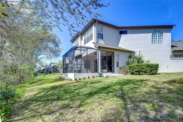 rear view of house featuring a sunroom, stucco siding, and a yard