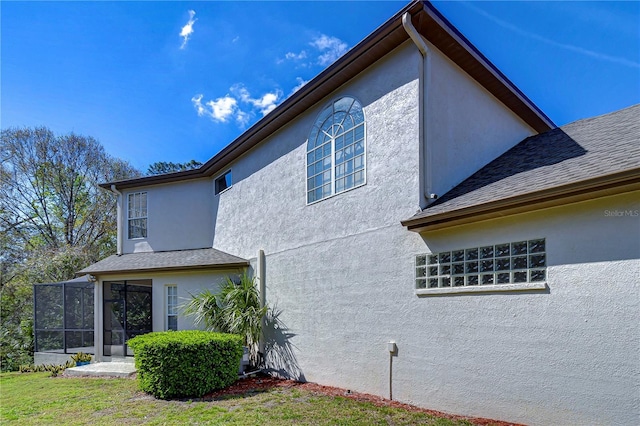 view of side of home featuring a shingled roof, a yard, and stucco siding