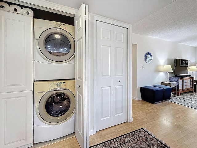 laundry room featuring laundry area, light wood-style flooring, stacked washer and clothes dryer, and a textured ceiling