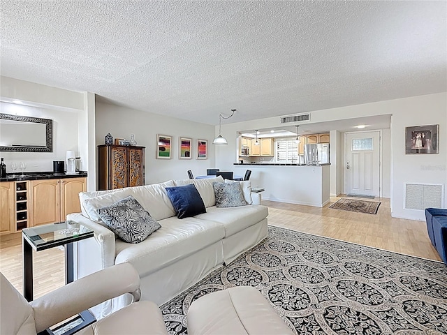 living room with light wood-type flooring, visible vents, wet bar, and a textured ceiling