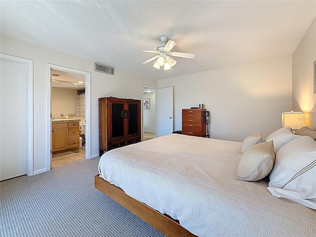 bedroom featuring a ceiling fan, visible vents, a textured ceiling, light colored carpet, and connected bathroom