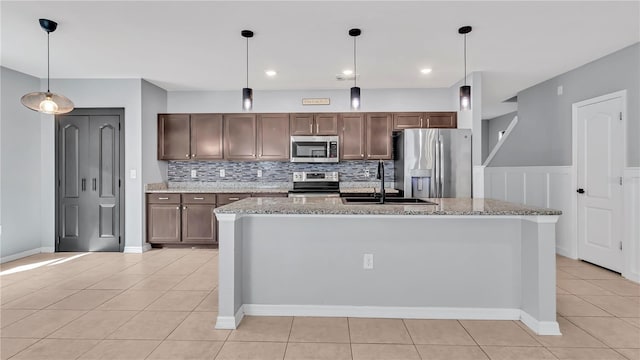 kitchen with a kitchen island with sink, a sink, tasteful backsplash, stainless steel appliances, and light tile patterned flooring