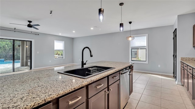 kitchen featuring baseboards, light stone countertops, decorative light fixtures, light tile patterned floors, and a sink