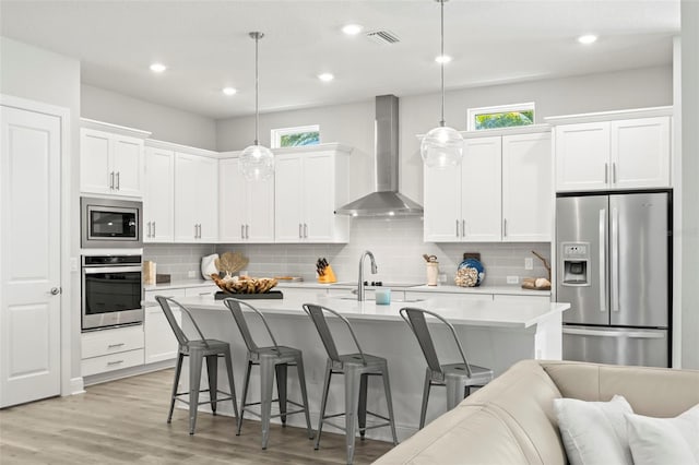 kitchen featuring wall chimney exhaust hood, appliances with stainless steel finishes, a kitchen bar, and light countertops