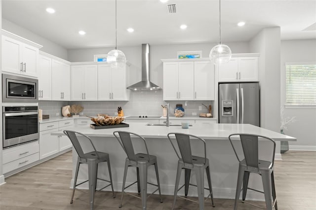 kitchen with stainless steel appliances, wall chimney range hood, light countertops, and visible vents