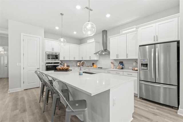 kitchen featuring light wood-style flooring, a sink, appliances with stainless steel finishes, wall chimney range hood, and backsplash