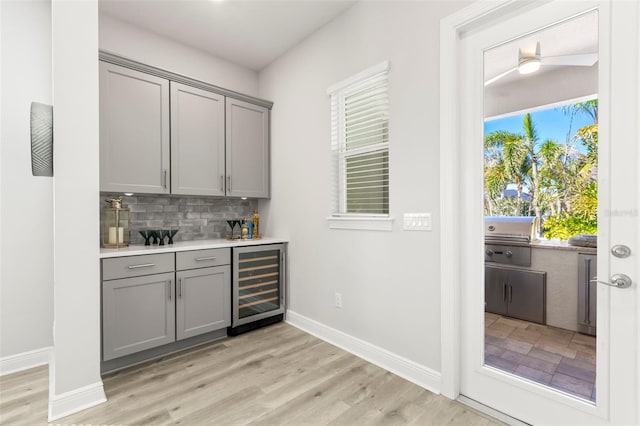 bar with beverage cooler, baseboards, decorative backsplash, and light wood-style flooring