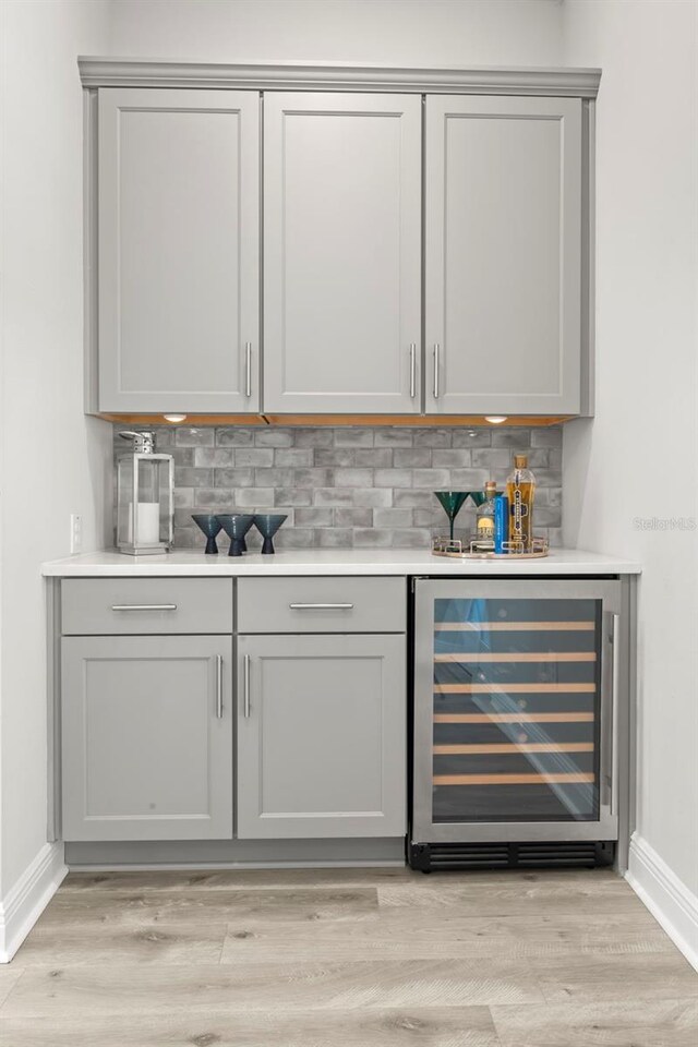 bar featuring light wood-style floors, beverage cooler, baseboards, and decorative backsplash