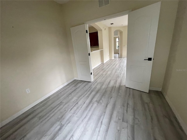 empty room featuring arched walkways, wood finished floors, visible vents, and baseboards