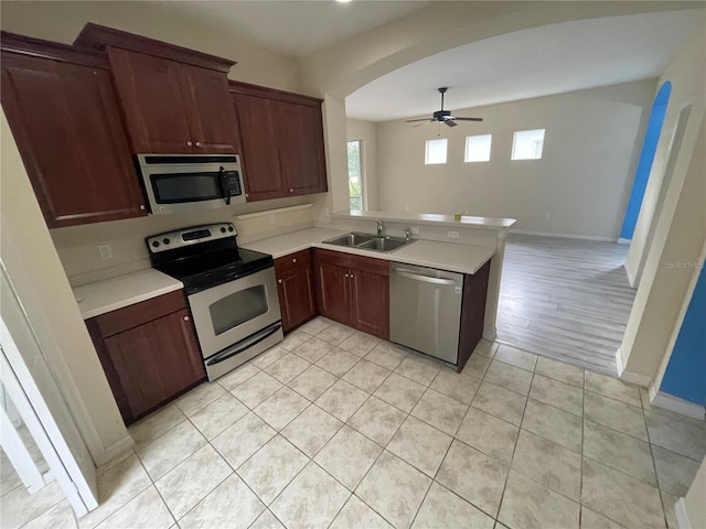 kitchen featuring arched walkways, stainless steel appliances, light countertops, a sink, and a peninsula