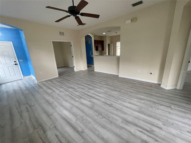 unfurnished living room with baseboards, visible vents, arched walkways, and wood finished floors