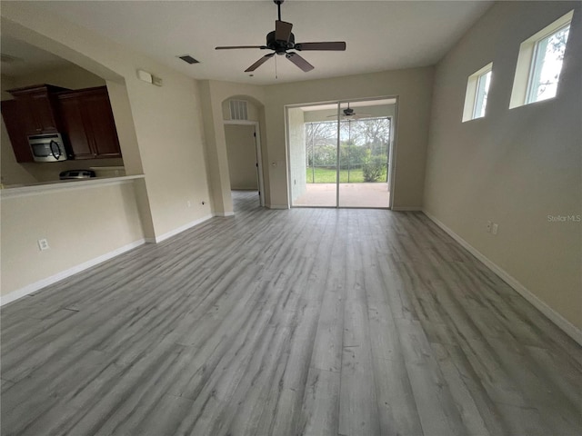 unfurnished living room featuring arched walkways, wood finished floors, visible vents, and baseboards