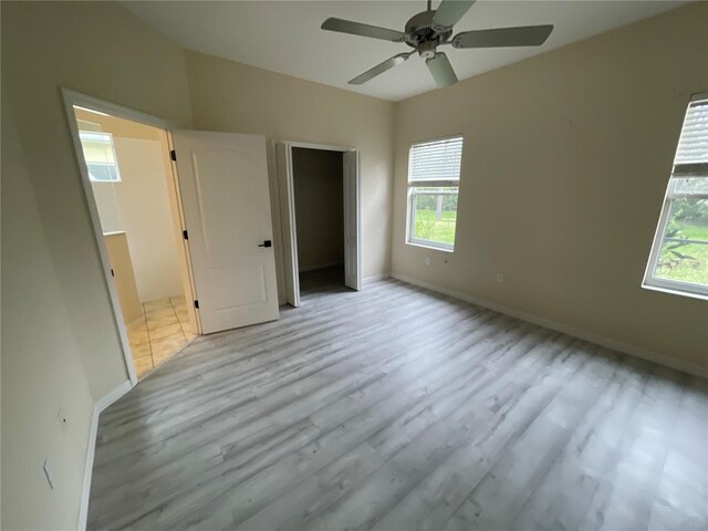 unfurnished bedroom with ceiling fan, multiple windows, light wood-type flooring, and baseboards