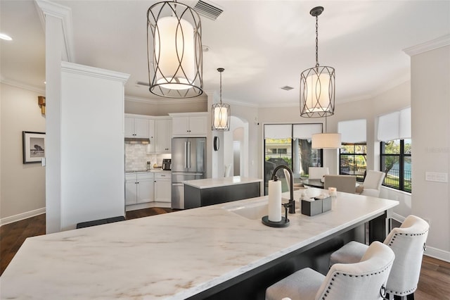 kitchen featuring arched walkways, a sink, visible vents, freestanding refrigerator, and a center island