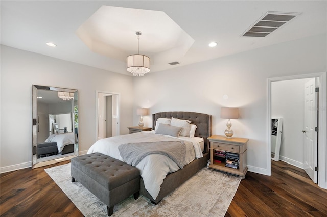 bedroom with baseboards, visible vents, wood finished floors, a tray ceiling, and recessed lighting