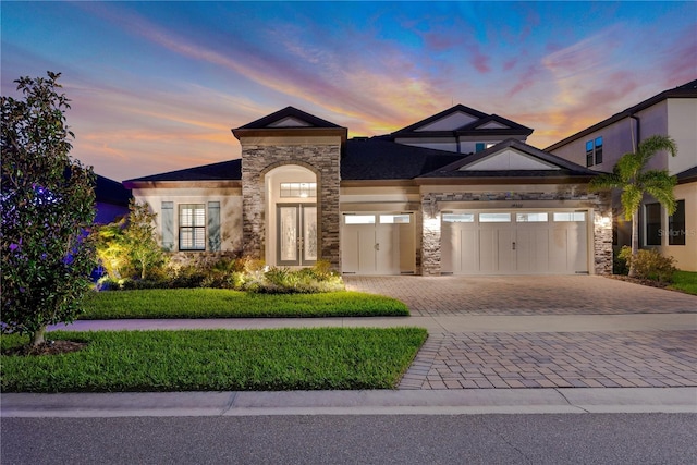 view of front of house with decorative driveway, stone siding, a garage, and stucco siding