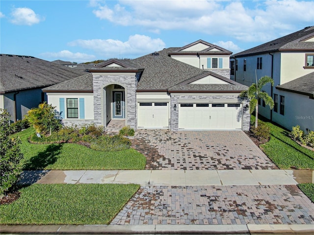 view of front of house with decorative driveway, stucco siding, a shingled roof, a garage, and stone siding