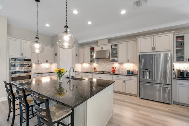 kitchen with visible vents, decorative backsplash, stainless steel appliances, under cabinet range hood, and a sink