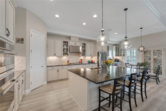 kitchen with tasteful backsplash, appliances with stainless steel finishes, a kitchen island with sink, and under cabinet range hood