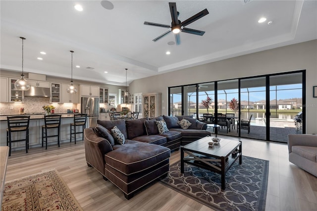 living room featuring light wood finished floors, ceiling fan, a tray ceiling, and recessed lighting