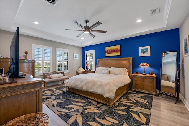 bedroom featuring light wood finished floors, visible vents, and a raised ceiling