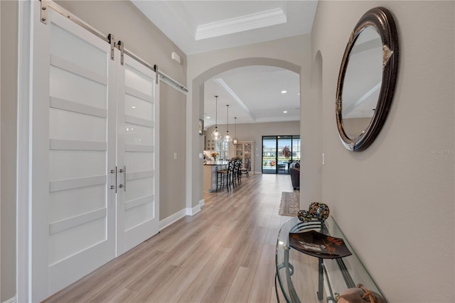 entryway with arched walkways, a barn door, light wood-type flooring, and crown molding