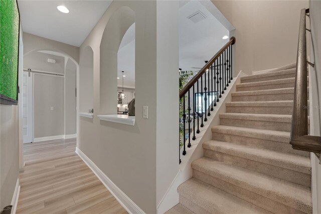 stairway featuring visible vents, baseboards, arched walkways, wood finished floors, and recessed lighting