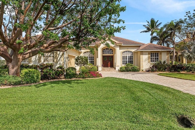 mediterranean / spanish-style home with a tile roof, driveway, a front lawn, and stucco siding