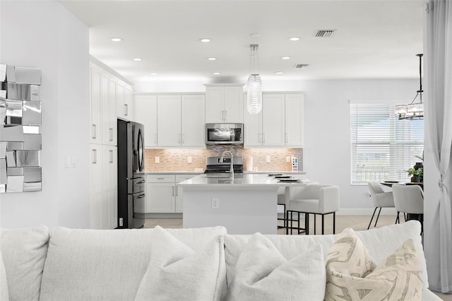 kitchen featuring appliances with stainless steel finishes, visible vents, an island with sink, and tasteful backsplash