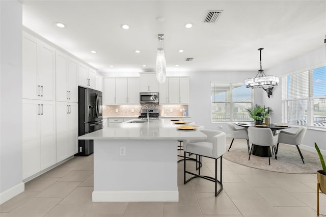 kitchen with tasteful backsplash, light countertops, stainless steel microwave, black fridge with ice dispenser, and a sink