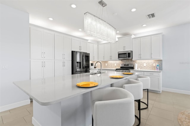 kitchen featuring a sink, visible vents, appliances with stainless steel finishes, decorative backsplash, and a kitchen bar