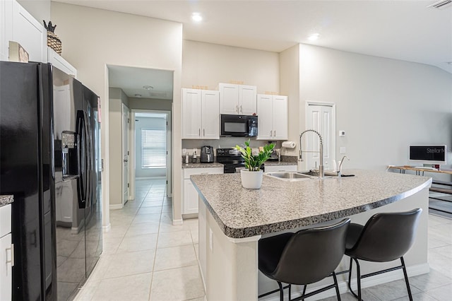 kitchen featuring a breakfast bar area, light tile patterned flooring, a sink, and black appliances