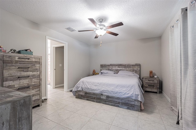 bedroom featuring a textured ceiling, light tile patterned floors, visible vents, baseboards, and a ceiling fan