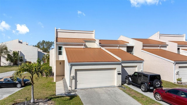 townhome / multi-family property with metal roof, a standing seam roof, driveway, and stucco siding