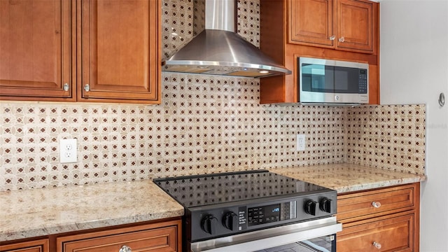 kitchen with brown cabinetry, decorative backsplash, electric range oven, wall chimney exhaust hood, and stainless steel microwave