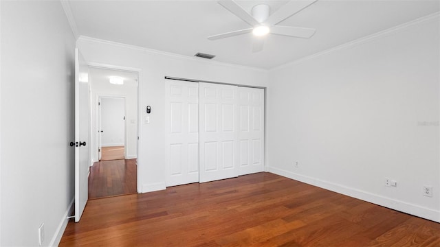 unfurnished bedroom with wood finished floors, visible vents, baseboards, a closet, and crown molding