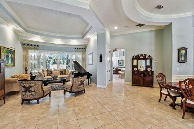 interior space with baseboards, a tray ceiling, ornamental molding, light tile patterned floors, and arched walkways