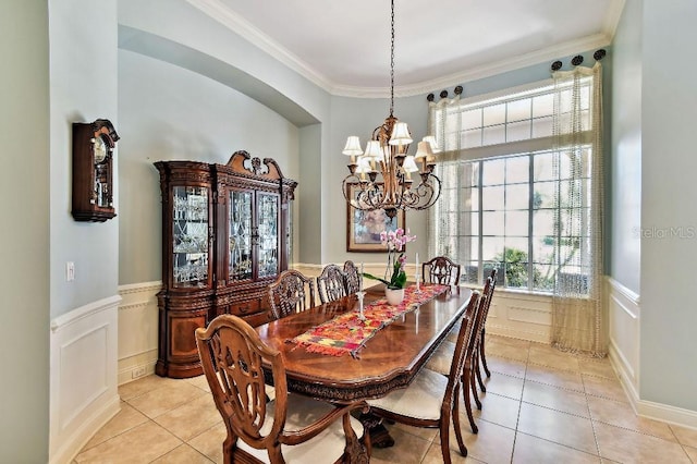 dining area with light tile patterned floors, a wainscoted wall, an inviting chandelier, crown molding, and a decorative wall