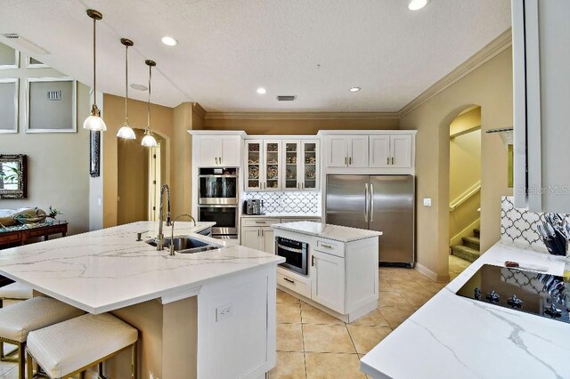 kitchen with arched walkways, a kitchen island with sink, a sink, decorative backsplash, and appliances with stainless steel finishes