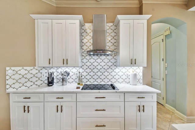 kitchen featuring light tile patterned floors, arched walkways, white cabinetry, wall chimney exhaust hood, and black electric cooktop