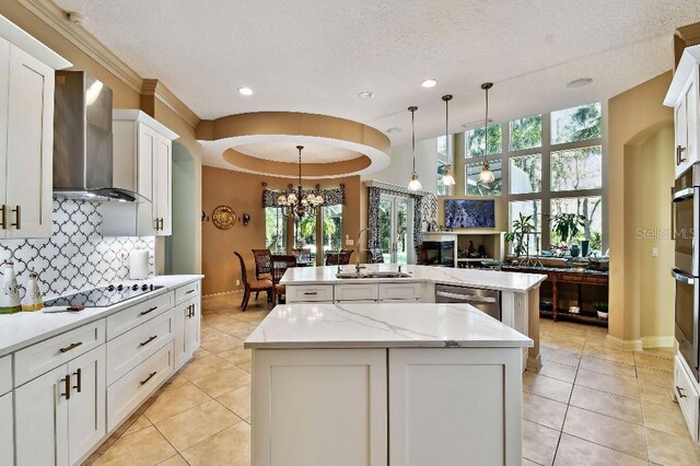 kitchen with tasteful backsplash, a kitchen island with sink, dishwasher, wall chimney exhaust hood, and a sink