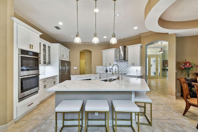 kitchen featuring a sink, wall chimney exhaust hood, arched walkways, and stainless steel appliances