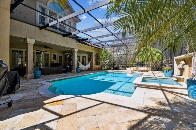 view of swimming pool with glass enclosure, a pool with connected hot tub, a ceiling fan, and a patio area