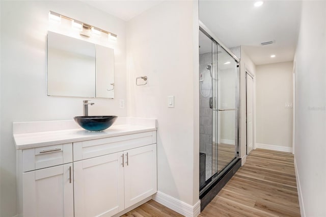 bathroom with a stall shower, visible vents, baseboards, wood finished floors, and vanity