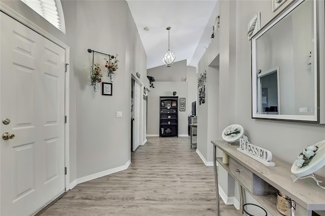 corridor featuring light wood finished floors, baseboards, high vaulted ceiling, and an inviting chandelier