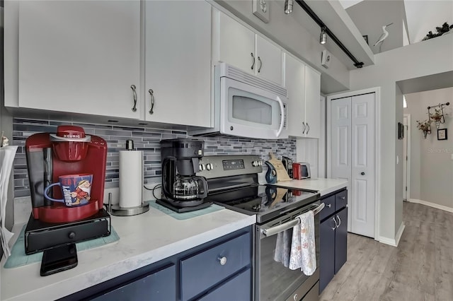 kitchen featuring white microwave, stainless steel electric range, light countertops, blue cabinetry, and backsplash